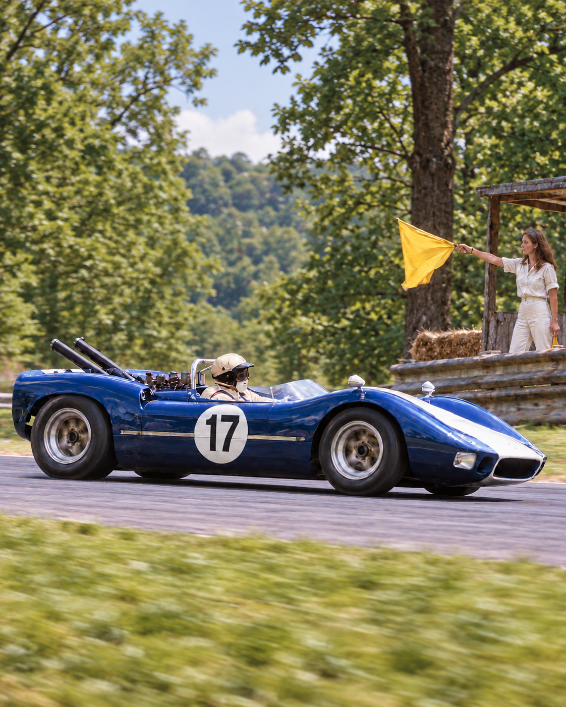 Blue-and-white number 17 sports racing car passing a young SCCA corner worker holding a yellow flag